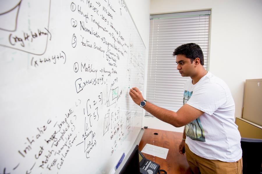 A student works through a programming challenge at a whiteboard.