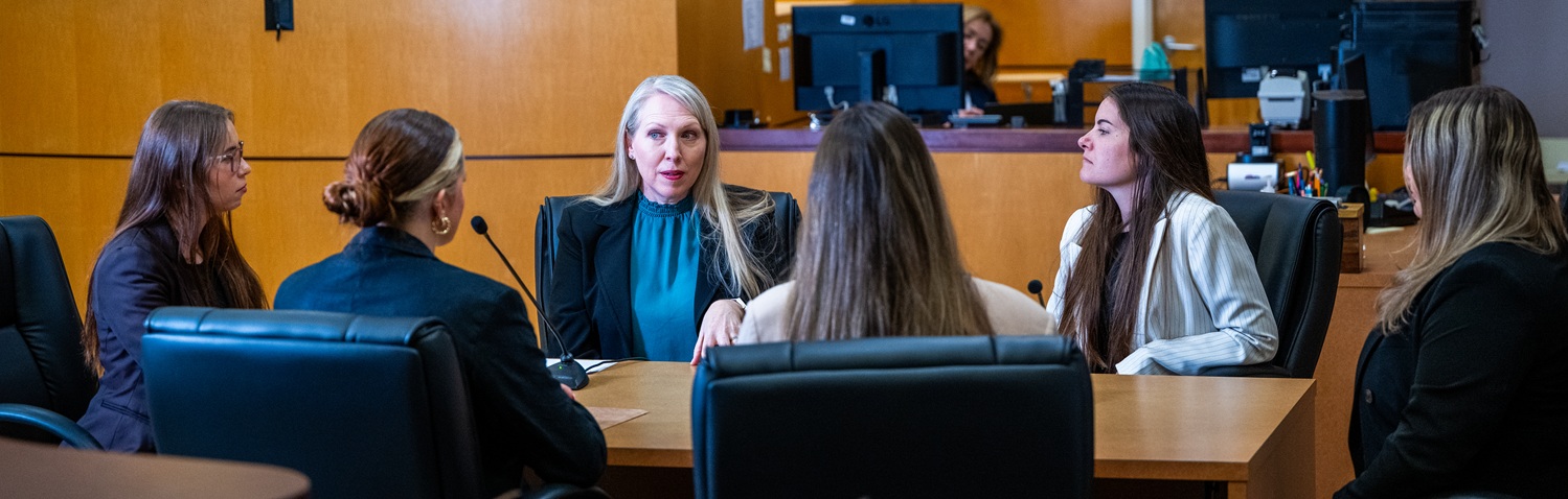 Students meet with their forensic psychology professor in a courtroom.