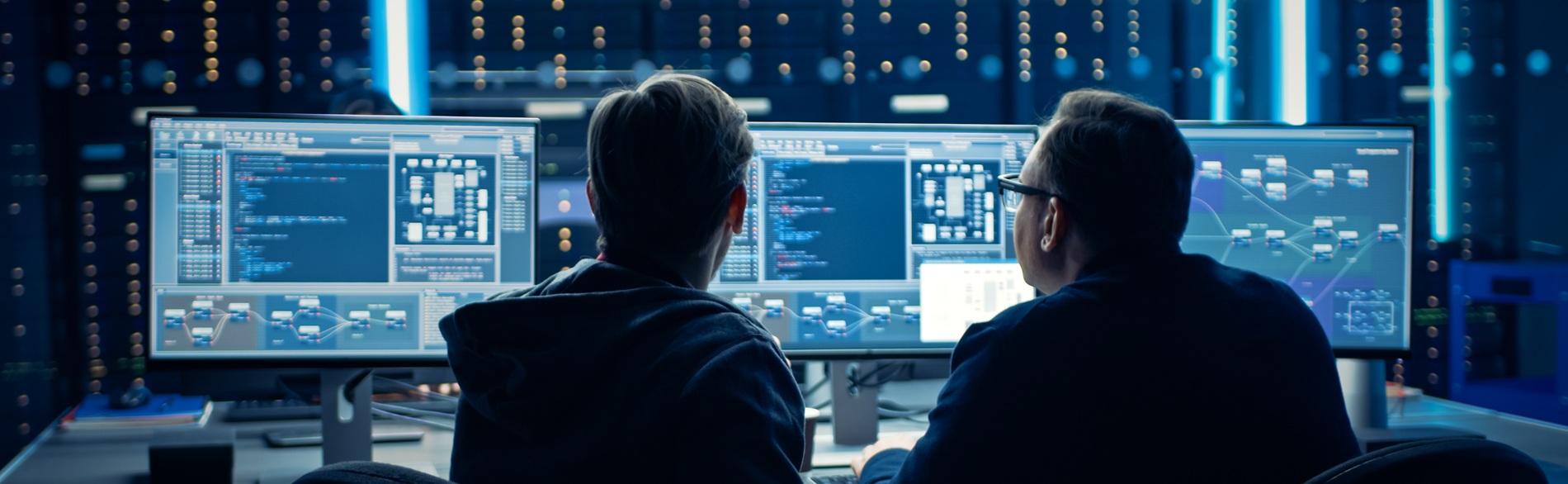 Two individuals examining code on computer screens in an IT environment