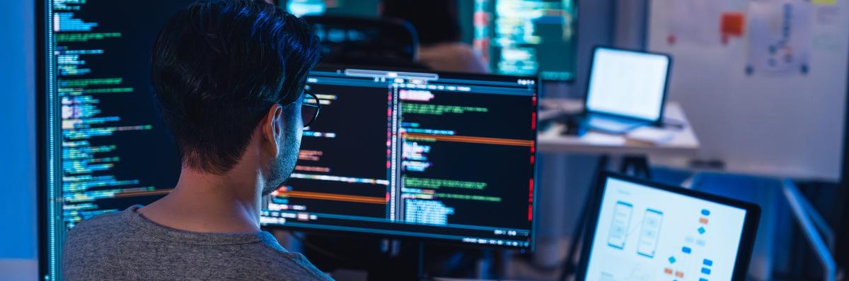 An individual looking at code on several screens