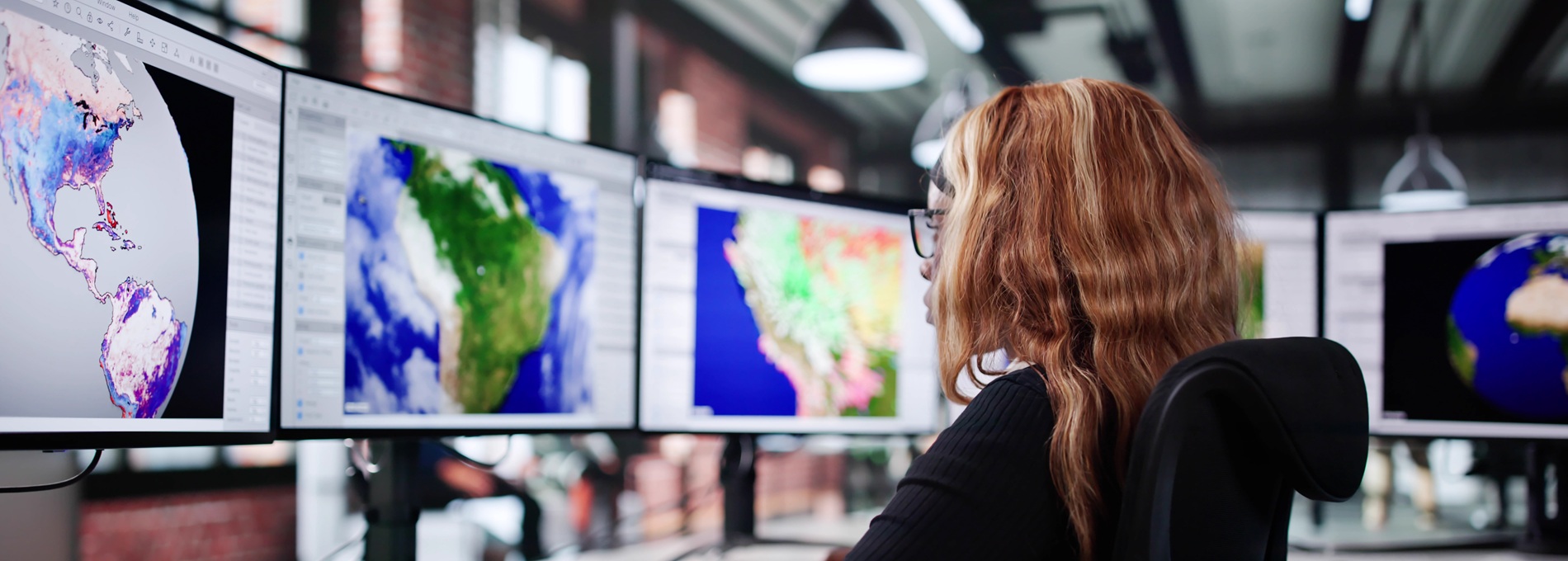A meteorologist at her desk viewing multiple monitors displaying weather data