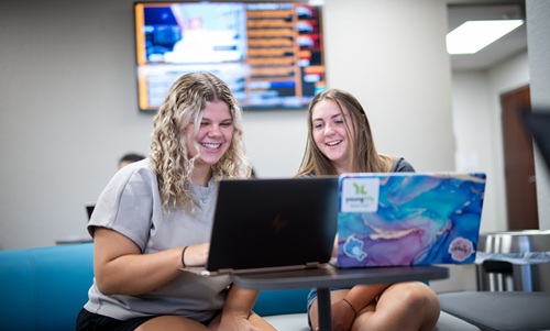 Two students working on laptops in the College of Business lobby