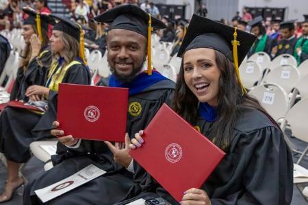 Two graduates holding their diplomas at commencement