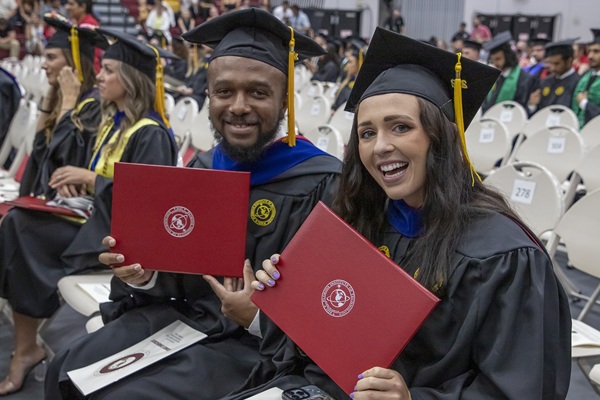 Two graduates holding their diplomas at commencement