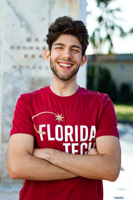 Smiling male student with arms crossed wearing red t-shirt with Florida Tech logo on front.