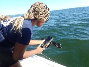 Female Florida Tech student leaning over side of boat with measurement instrument