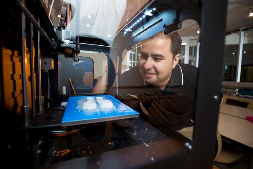 A male student looking closely at a 3D printer.