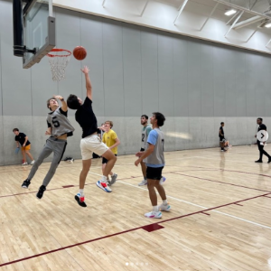 Students playing in an intramural basketball game. One student attempts a layup as others defend.