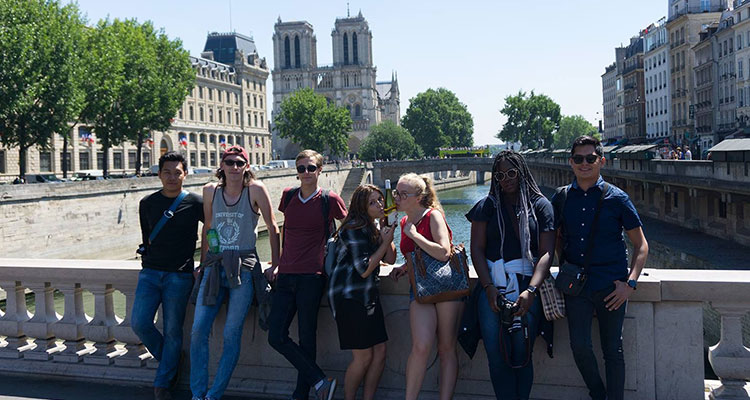 Students standing on a bridge in front of the Notre Dame Cathedral